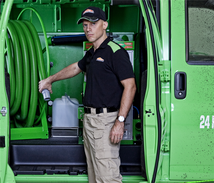 SERVPRO tech standing in front of a SERVPRO van holding water cleanup tools